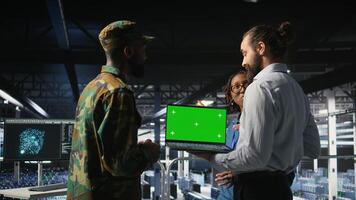 Army tech specialist in data center and coworkers using green screen laptop to troubleshoot military computer systems. Soldier and command center server room admins using chroma key notebook, photo