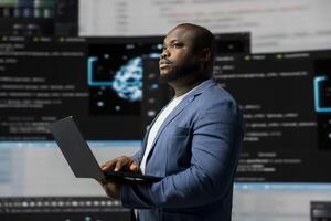 African american coder expert immersing in software development for a high tech work environment, focused on laptop screen. Engineer enjoying coding life and IT cloud computing. photo