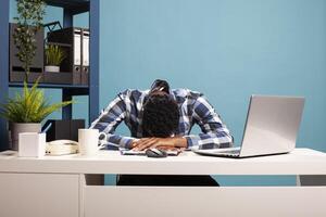 Overworked male entrepreneur collapsed on his office desk from fatigue after long work hours, showing stress and burnout. Exhausted businessman resting head on table from tiredness. photo