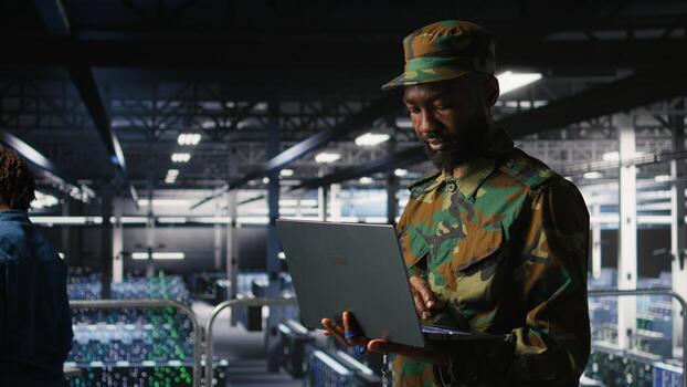 Army information technology specialist in data center troubleshooting military computer systems and networks using laptop. Soldier in command center server room using notebook, photo