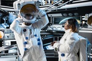 Researcher travelling in space with starship putting helmet on, talking with colleague, conducting scientific experiments. Scientist dressing in equipment, chatting with coworker during cosmic journey photo
