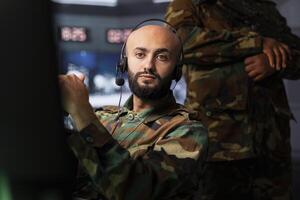 Military agent in war room doing reconnaissance mission, using headset gear. Army expert monitoring counterinsurgency enemy fighters using telecommunication systems to intercept calls photo