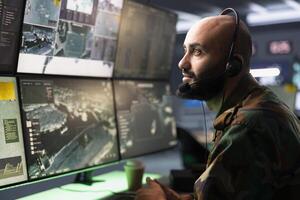 Counterintelligence agency agent relays information from army intelligence analysts to front lines soldiers. Man in camouflage uniform doing satellite communications, talking in mic photo