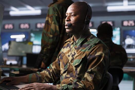 Agent in command post uses gear to identify threats from enemies. African american army operator in base of operations uses headset mic to communicate information to generals on war front line photo