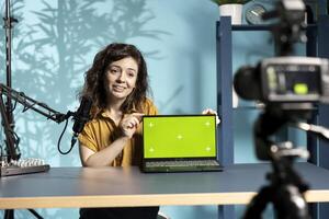 Cheerful woman in studio filming tech tutorial on how to do maintenance on broken chroma key laptop. Jolly online show host teaching subscribers how to open and fix defective green screen notebook photo