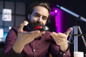 Influencer happily promoting neon lit gaming mouse from sponsor to audience. Joyful content creator paid by brand to showcase computer peripheral device, recording with professional microphone photo