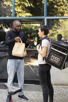 Black male client holding a takeout package with the wrong order, confronting the delivery worker about a shipping problem. The incorrect meal causes tension during failed courier service. photo