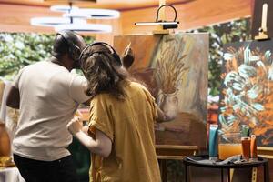 Talented artist and her apprentice applying watercolor paint on canvas, working together to create a beautiful nature inspired masterpiece in atelier. Two people painting a colorful scene. photo