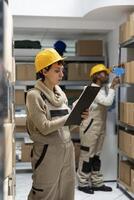 Woman warehouse worker ensures inventory management with boxes on racks, focusing on goods dispatch and quality control operations. Pallets stacked in the industrial storehouse. photo