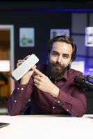 Joyful influencer doing technology review of wireless portable speaker for internet platforms channel. Influencer pointing to music playing gear to his subscribers, recommending it photo