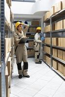 Female employee counting supplies boxes on racks for daily depot operations, focusing on goods dispatch and quality control. Pallets and boxes stacked in the industrial warehouse. photo