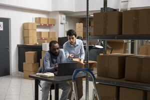 Multiethnic staff working on a local business express delivery with orders, surrounded by taped boxes and inventory shelves in a small warehouse. Industrial distribution logistics. photo
