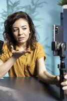 Influencer in home studio recording live broadcast using smartphone on selfie stick, reading messages from fans. Media star hosting q and a session, filming with phone, answering questions photo
