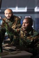 Military officers looking at radar surveillance footage in base of operations to allocate resources to units based on mission needs. Agent and coworker in control center examining data on displays photo