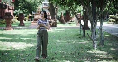 Relaxed Asian woman listening to music on wireless headphones over a mobile app while walking leisurely in a quiet place. video