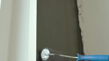 Close-up of paint roller applying dark color to wall during interior renovation. Concept of DIY painting, home improvement and redecoration in modern apartment video