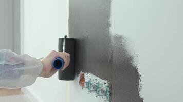 cClose up of person using roller to paint wall black near electrical sockets during home renovation video
