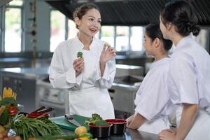 Professional chef is teaching young culinary class student to prepare fresh broccoli as ingredient for the meal inside the restaurant kitchen for fine dining gourmet and cooking school photo