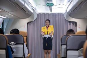 African flight attendant is demonstrating safety procedure using life jacket before taking off inside airplane for cabin crew and airline business photo