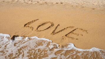 Love written on sandy beach with ocean waves approaching photo