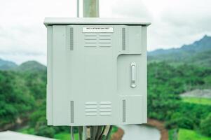 Industrial control cabinet at hydroelectric dam crest with modern electrical equipment and green forest mountain background. Sustainable renewable energy infrastructure. Power monitoring system. photo