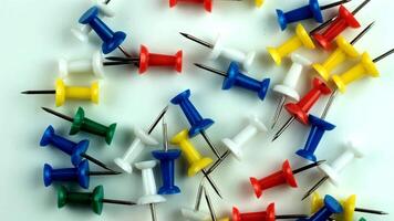 Colorful push pins scattered on a white surface. The pins are in various colors including red, yellow, green, blue, and white. They are commonly used for pinning notes. video
