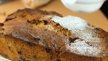 A freshly baked loaf of cake with a dusting of powdered sugar on top. The cake has a golden-brown crust and a moist interior, placed on a wooden surface. video
