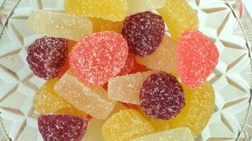 Colorful gummy candies in various shapes and sizes arranged in a decorative bowl. The candies include red, yellow, orange, and purple varieties. video
