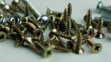 A close-up view of various screws and nuts in different metallic colors. The scene includes a mix of silver, gold, and bronze screws scattered on a surface. video