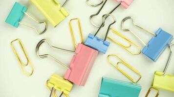 Colorful paper clips and binder clips scattered on a white surface. The scene features various sizes and colors, including pink, blue, yellow, and green. video