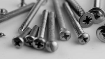 A collection of various metal screws and nuts scattered on a white surface. The screws vary in size and type, showcasing their threaded designs. video