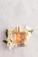 A bottle of perfume with a delicate scent of jasmine lies on white jasmine flowers. Marble background. top view. A copy space. A blank bottle mockup. photo