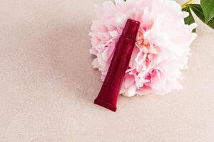 An unnamed tube of cosmetics leaned on a large gorgeous pink peony flower. Beige stone background. A copy of the space. Blank tube layout. photo