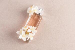 An elegant bottle of cosmetics, cologne, perfume lies on a stone beige background with white jasmine flowers. Upper view. A copy of the space. photo
