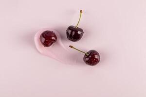 Beautiful brushstroke of cosmetic texture of balm, mask, lip gloss with ripe juicy cherries on pink background. top view. cosmetic layout. copy space. photo