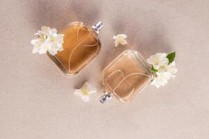 Two identical transparent perfume bottles lie on a beige stone background among white jasmine flowers. delicate aroma. Empty bottle layout. top view. photo