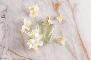 A glass transparent perfume bottle of lies on an abstract marble background with white jasmine flowers. top view. A blank bottle mockup. A copy space photo