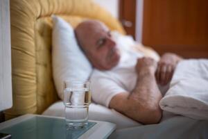 Elderly male resting peacefully in bed with selective focus on the water glass, emphasizing self care and morning refreshment. photo