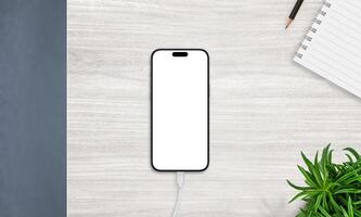 Top view of smartphone on charger with blank screen, placed on desk with notebook and plant. Ideal for productivity and app mockups photo