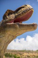 Artificial dinosaur tyrannosaurus, close-up of dinosaur head against sky background. With copy space. Jurassic Park with huge figure of predatory tyrannosaurus. You can see dinosaur teeth. vertical photo