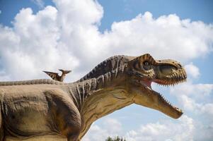 Artificial dinosaur tyrannosaurus, close-up of dinosaur head against sky background.Two dinosaurs. Pterodactyl and tyrannosaurus. One huge dinosaur and the other smaller. Photo in a cold shade