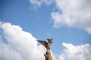 Pterodactyl against the sky. A single dinosaur statue sits on a tree trunk against the backdrop of clouds. copy space. horizontal photo. Clouds in a blue cloudy sky. High quality photo