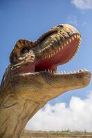 Artificial dinosaur tyrannosaurus, close-up of dinosaur head against sky background. With copy space. Jurassic Park with huge figure of predatory tyrannosaurus. You can see dinosaur teeth photo