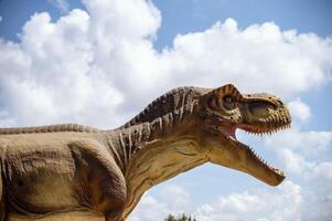 Huge dinosaur tyrannosaurus, close-up of dinosaur head against sky and clouds. With copy space. Dinosaur in profile, with open mouth against bright background photo