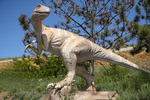 Dinosaur statue with a long tail. Dinosaur figure among trees in nature in the park. Against the background of blue sky and trees. copy space. photo