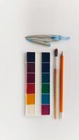 School supplies flat lay with watercolor paints, compass, pencil and brush on white background. Creative tools for drawing and learning. Back to school and artistic education concept. photo