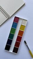 Top View of Watercolor Paint Set with Brush and Spiral Notebook on White Background. Artistic Supplies for Back to School and Creativity. photo