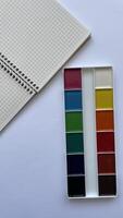 Top View of Watercolor Paint Set and Spiral Notebook on White Background. Back to School Creative Concept. Stationery for Drawing and Education. photo