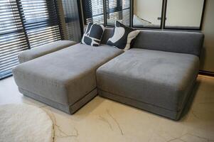 Ergonomic gray, velour sofa standing near a large window with wooden blinds with copy space photo