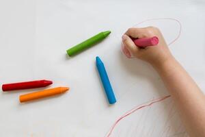 Child coloring with bright crayons on white paper photo